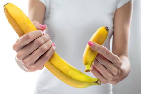 Bananas of different sizes in the hands of a slender girl. Concept. Size matters.の写真素材