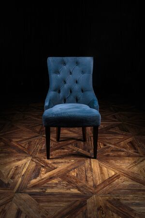 armchair, covered with gray velvet, standing in a circle of light on a wooden parquet floor with a beautiful geometric pattern on a dark backgroundの写真素材