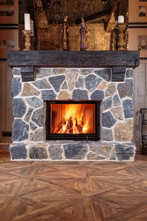 blazing fire in the massive fireplace of hewn stone on a beautiful wooden floorの写真素材