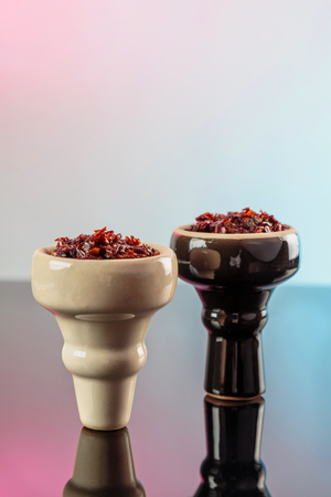 shisha with apple flavor in glossy white and black bowls on a dark mirror surface with colored...