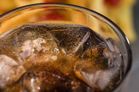 fizzy drink with ice in a glass on the background of a plate with fried potatoes.の写真素材