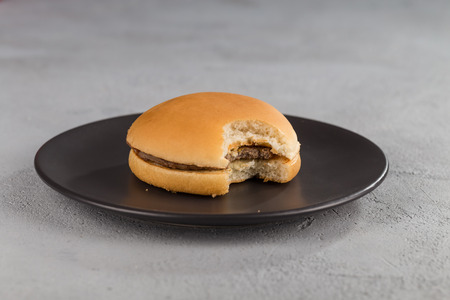 fast food with delicious bitten hamburger on a black ceramic plate.の写真素材