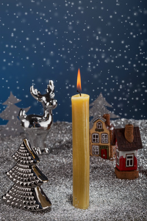 Burning candle on the background of Christmas snowfall and toy figures. Merry Christmas and happy holidays Christmas story concept.の写真素材