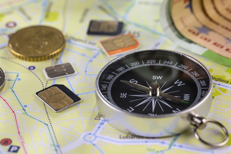 Close-up gsm cards of different sizes lie on the city map surrounded by coins, Euro banknotes and compassの写真素材