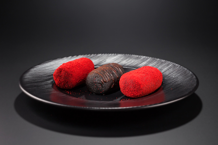 three miniature cakes, two with red sprinkles and one chocolate, on a black plate.の写真素材