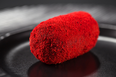 Close-up miniature cake-potatoes with red sprinkles on a black plateの写真素材