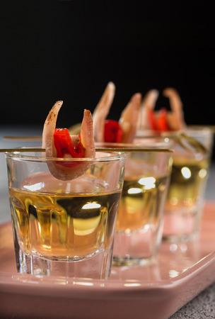 Close-up shot of three glasses of Golden tequila with tapas on skewers with dried meat, baked bell pepper and pine nuts.の写真素材
