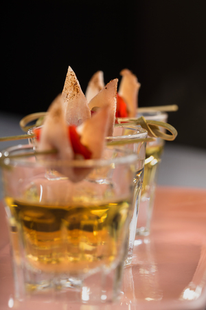 Close-up shot of three glasses of Golden tequila with tapas on skewers with dried meat, baked bell pepper and pine nuts.の写真素材