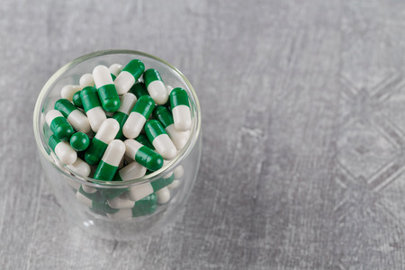 close-up of white-green pills in glass Cup on grey backgroundの写真素材
