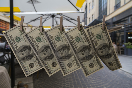 close-up hundred dollar bills, attached with clothespins to a rope, hang against the background of...