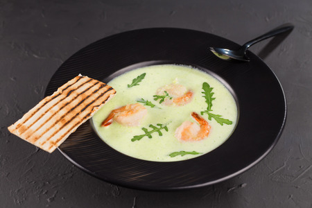 Cream broccoli soup with shrimp in a beautiful black plate on a dark background. Seafood dish. Selective focus.の写真素材