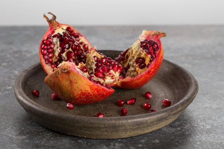 Open ripe pomegranate fruit on an old clay plate. Horizontal.の写真素材