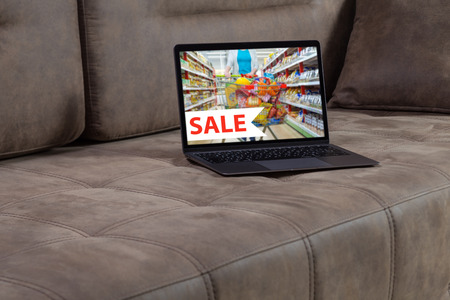 Open modern laptop with the inscription sale on the screen stands on a beautiful sofa. Shop on the sofa. Buying on the Internetの写真素材