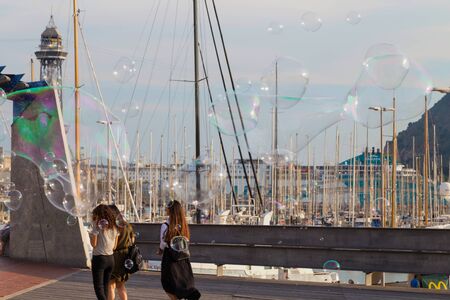 Soap bubble show on the pier in Barcelona, Spain, 28.06.2018. Happy children play outdoors in the background of moored yachts.のeditorial素材