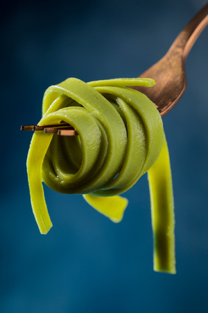 Green spaghetti on a fork on a beautiful colored background.の写真素材