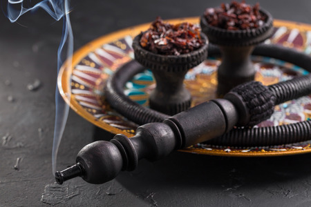 Shisha in black burnt ceramic bowls stands on a beautiful plate with a bright Oriental pattern on a dark background. Traditions of hookah Smoking.の写真素材