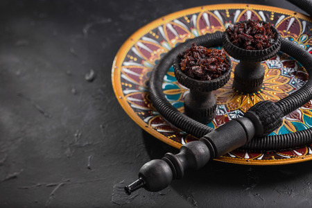 Shisha in black burnt ceramic bowls stands on a beautiful plate with a bright Oriental pattern....