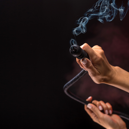 Hookah mouthpiece with a stream of smoke in a beautiful female hand on a dark background. Selective focus.の写真素材