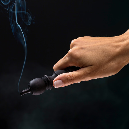Hookah mouthpiece with a stream of smoke in a beautiful female hand on a dark background. Selective focus.の写真素材