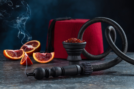 Shisha for hookah in a black burnt bowl on a beautiful dark background with sliced red oranges.の写真素材