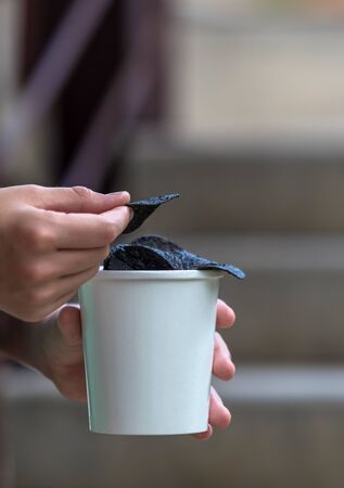 Black chips. Black potato chips in the hands of a teenager on the background of a sunny summer landscape.の写真素材