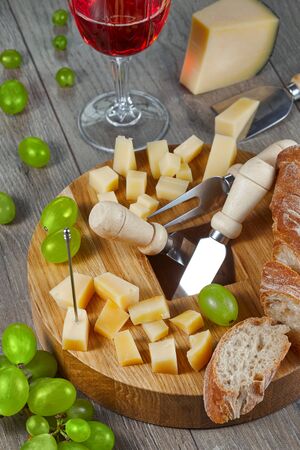 Cheese of different varieties, cut for tasting on a cutting Board with grapes, bread and a glass of red wine. Close up.の写真素材