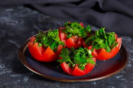 Tomato halves with finely chopped parsley lie on a plate on a dark background. Healthy diet.の写真素材