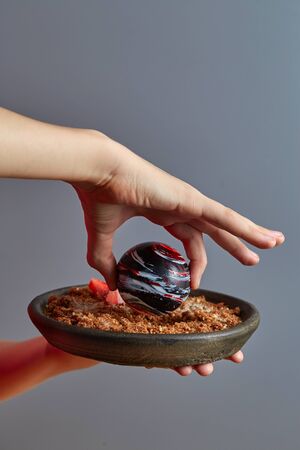 Close-up of an exquisite dessert of a planet-like colored chocolate ball in the hands of a boy, with...