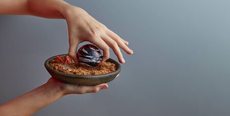 Close-up of an exquisite dessert of a planet-like colored chocolate ball in the hands of a boy, with caramelized dark bread with almond crumbs, garnished with strawberries and mint. Copy space.の写真素材