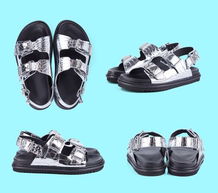 Pair of modern sandals made of textured crocodile skin with a mirror Shine with metal clasps and a black rubber sole, isolated on a sea wave background with a shadow.の写真素材