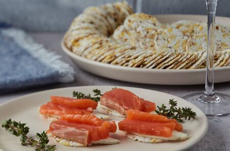 Canapes with salmon on a plate decorated with thyme sprigs, against the background of a dish with...
