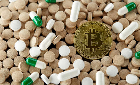 Golden bitcoin lies among randomly scattered tablets and capsules of various colors and sizes....