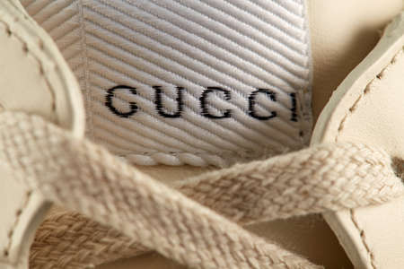 Close-up of the Gucci logo, embroidered with text on the tongue of a beige sneakers with lacing....