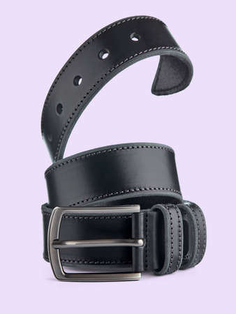 Black leather belt with a metal buckle, beautifully twisted in a vertical spiral, is highlighted on a light purple background.の写真素材