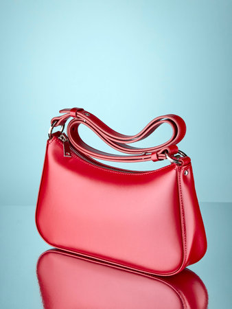 Fashionable handbag made of glossy red leather, standing on a mirror surface, on a pale blue background with a reflection. Copy space.の写真素材