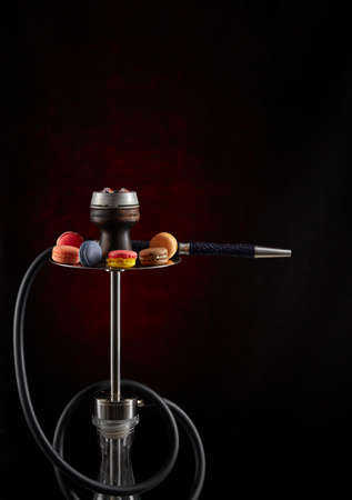 Modern hookah decorated with macaroon of various colors on a dark background. Vertical inage. The...
