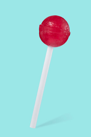 Close-up of a red lollipop in the shape of a ball on a stick, isolated on a beautiful turquoise background with a shadow. Sweets.の写真素材