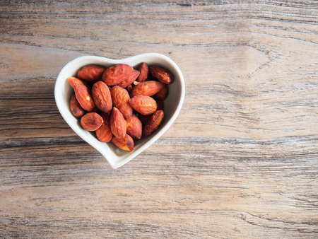 Roasted almond in heart bowl shape on wooden table.の写真素材