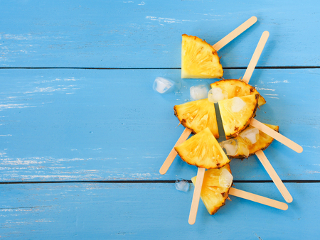 Slice pineapple popsicle sticks and ice  on blue wooden table with copy space for summer fruit party concept.の写真素材