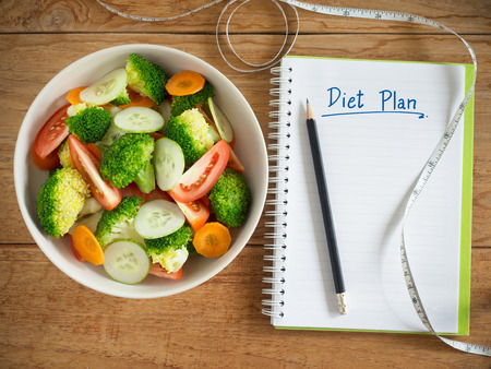 Mixed vegetables salad bowl and diet plan notebook with measuring tape for eat healthy food concept.の写真素材
