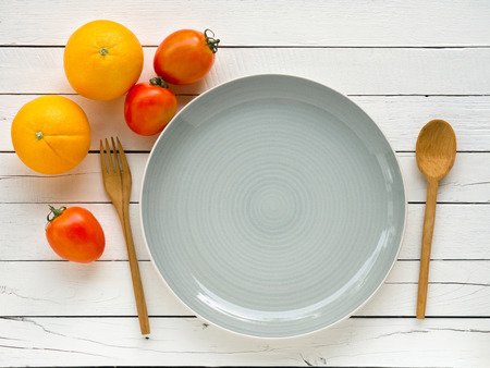 Orange,tomato and empty dish on white wooden table for eating healthy food concept.の写真素材