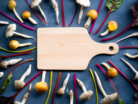 Empty wooden cutting board in center with organic rainbow swiss chard vegetable and mushroom for cooking concept  background.の写真素材