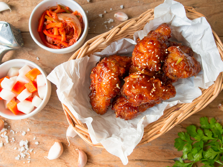 Deep fried chicken wing with garlic sauce in Korean style serve with kimchi and pickled radish in top view on wooden table for asian food concept.