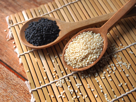 White and black sesame seeds in wooden spoonの写真素材