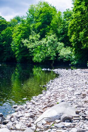 River Kent running over the rocks and pebbles with tree lined banks in summerの写真素材