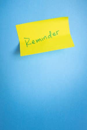 Reminder sticky note on blue light background. Minimalist concept. Copy space