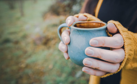 Young woman hands holding a blue mug of tea outdoorの写真素材