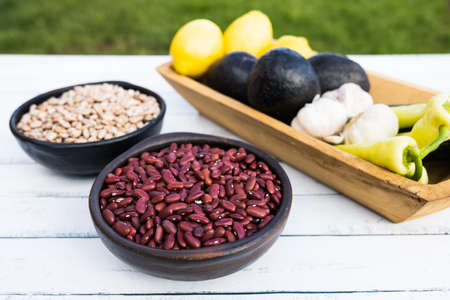 Beans in dark bowls on wooden background. Avocados, garlic, lemons and green chilies.