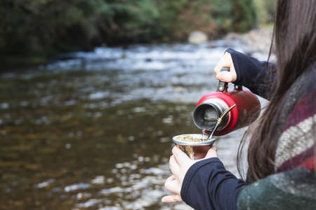 Young woman serving mate in a natural space. Beside a river. Latin beverage.