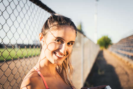 Smiling caucasian young active woman looking at the camera and setting a music playlist on her smartphoneの写真素材